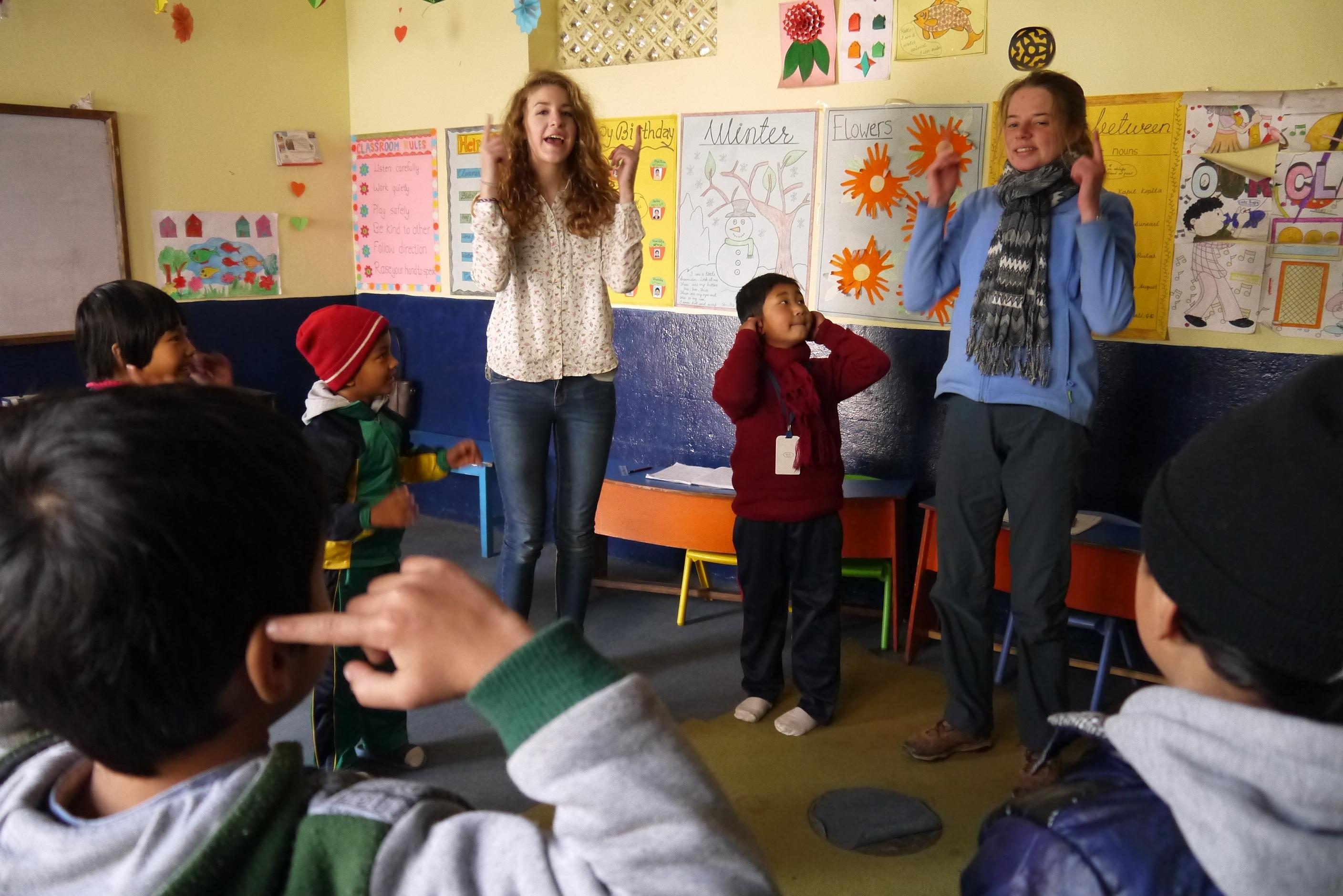 Two female Projects Abroad Care volunteers lead an interactive activity with children during a childcare work placement in Nepal. Female Childcare volunteer working with children in Nepal are leading physical activitie in a day care centre during a project.